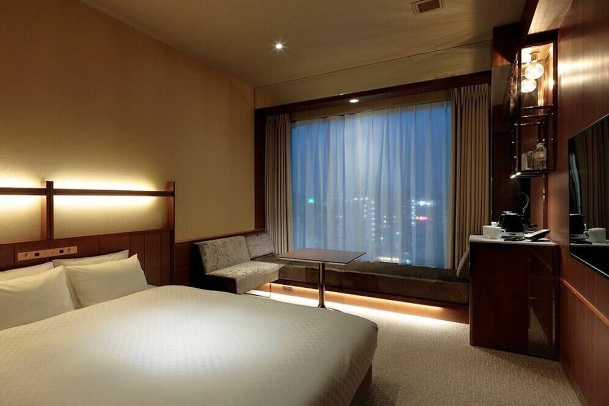 A hotel room with a large bed, a sofa, a small table, a TV, and a window with curtains.