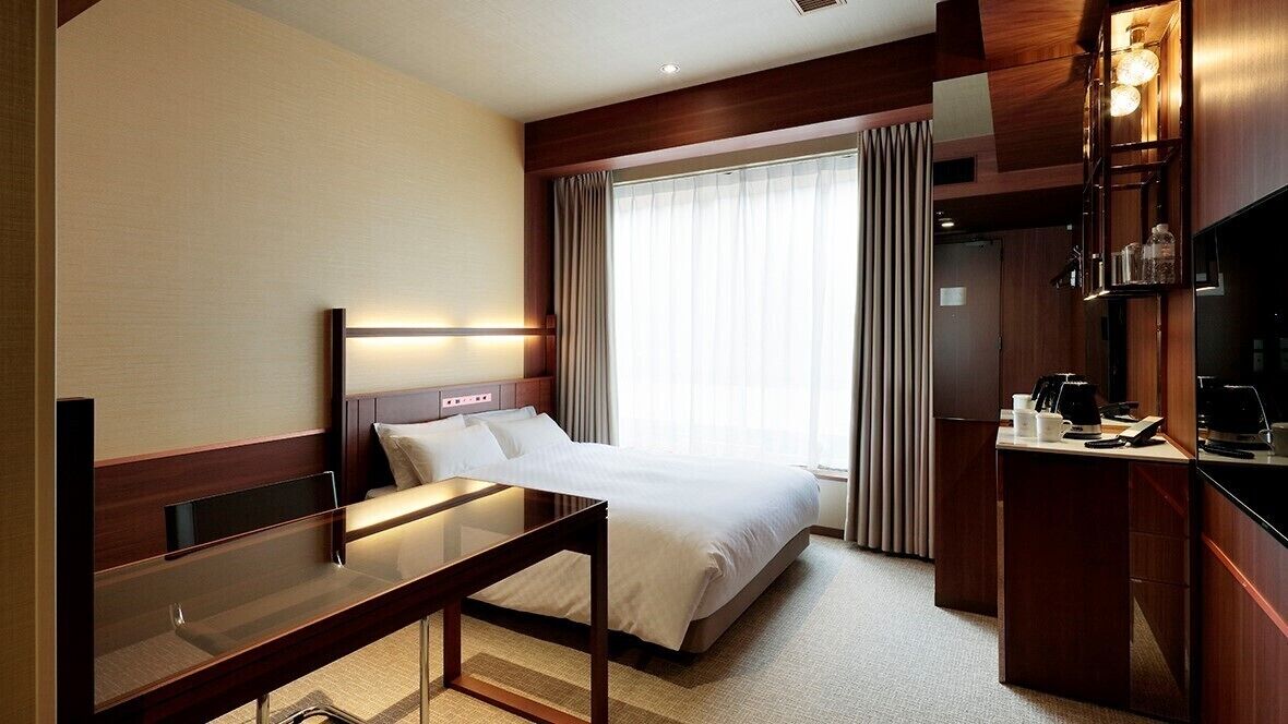 Una habitación de hotel con cama, mesita de noche, escritorio y televisor.