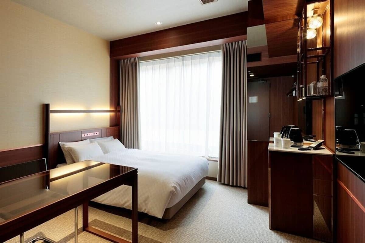 A hotel room with a bed, bedside table, desk, and a television.