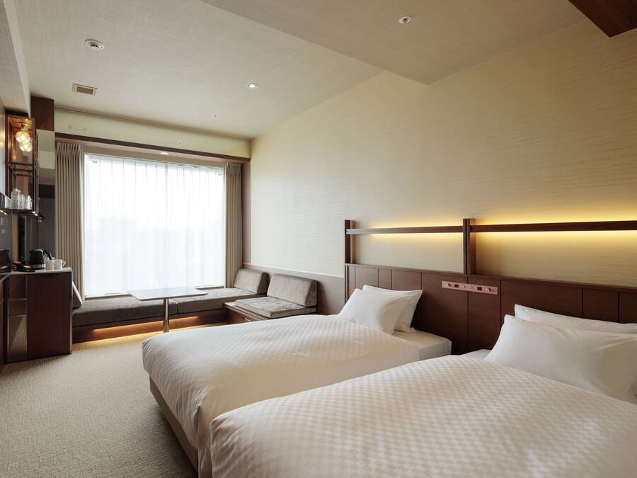 A hotel room with two beds, a desk, a chair, a TV, and a window with curtains.