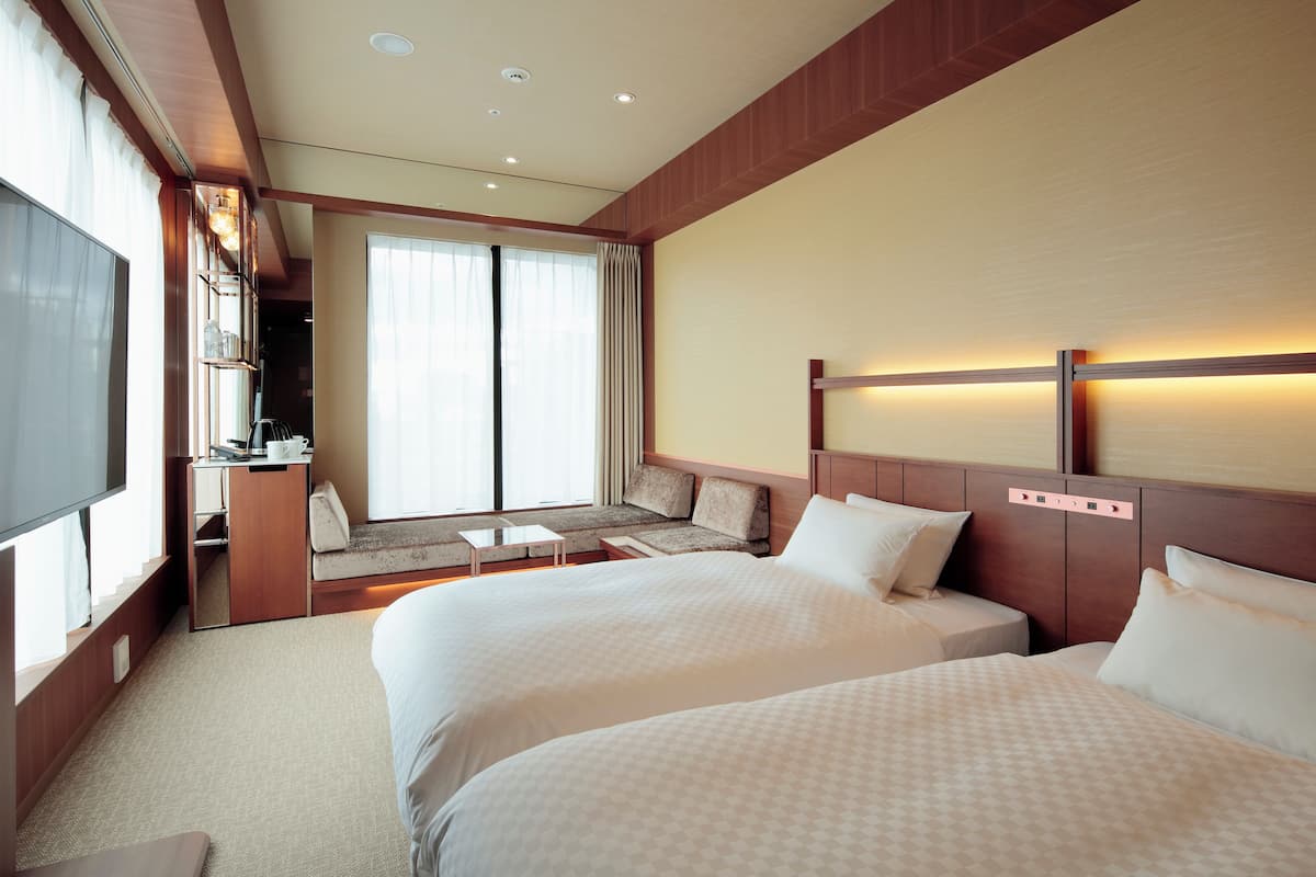 A hotel room with two beds, a seating area with a view, and a TV.
