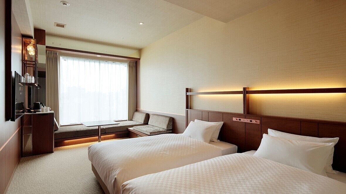 Habitación de hotel con dos camas, un escritorio, un televisor y una ventana con cortinas.