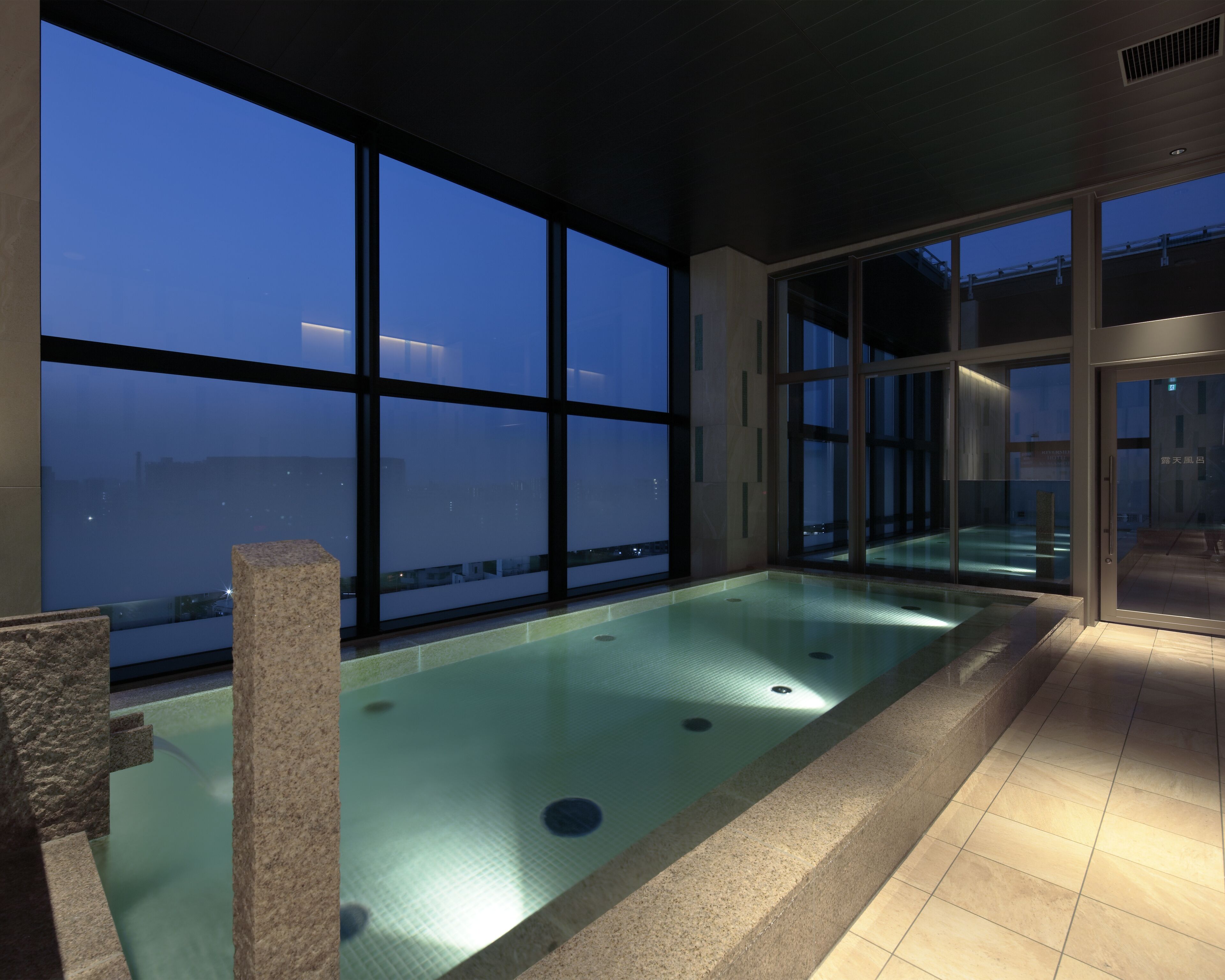 Piscina interior moderna con amplias ventanas y vistas de la ciudad al atardecer.