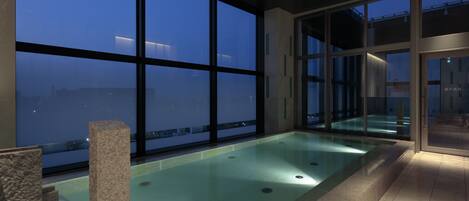 Piscina interior moderna con amplias ventanas y vistas de la ciudad al atardecer.