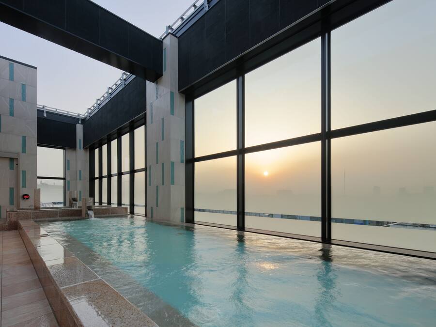 A modern indoor swimming pool with large windows and a view of the sunset.