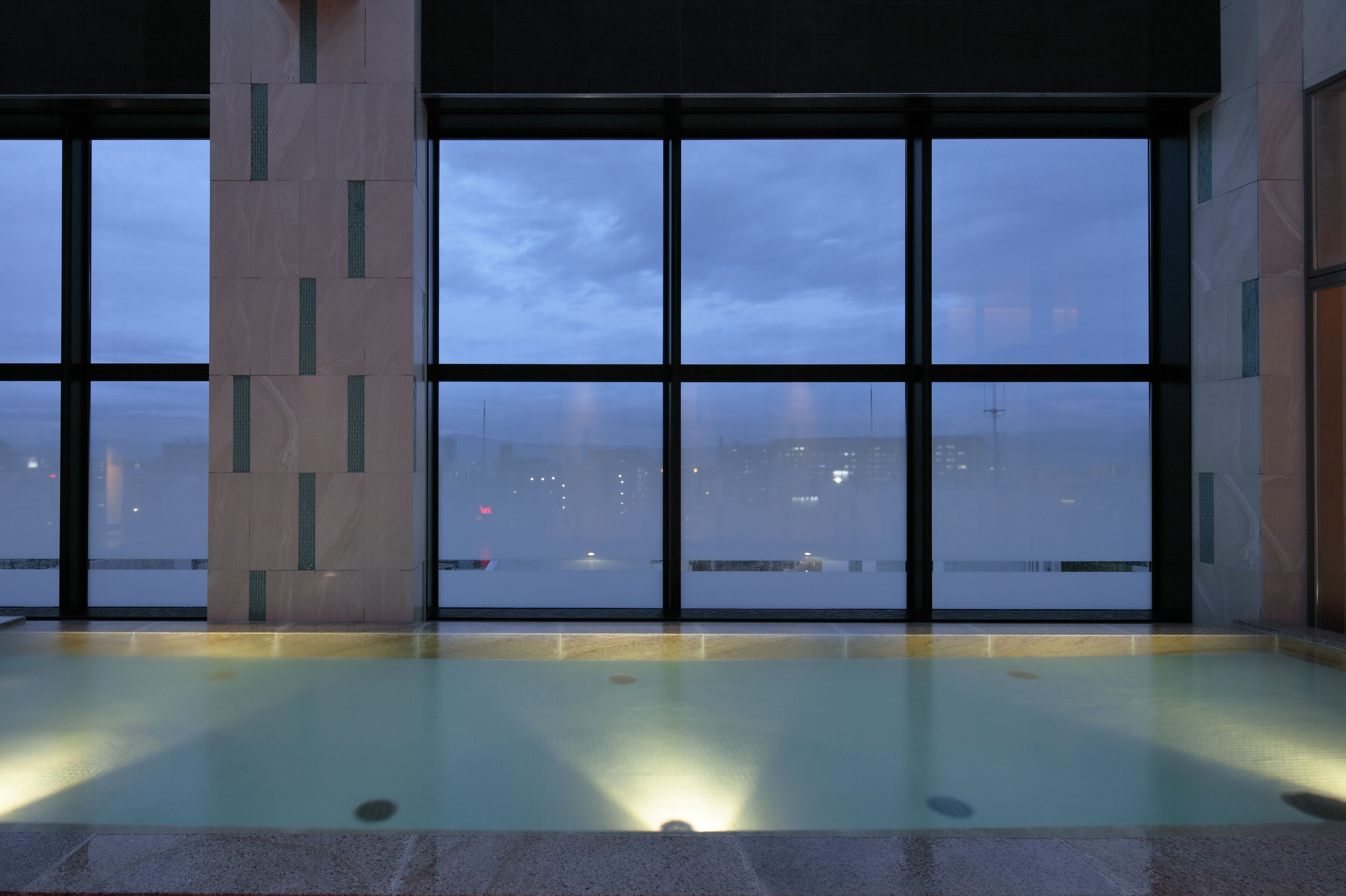 Uma piscina coberta ampla com vista para a cidade através de grandes janelas.