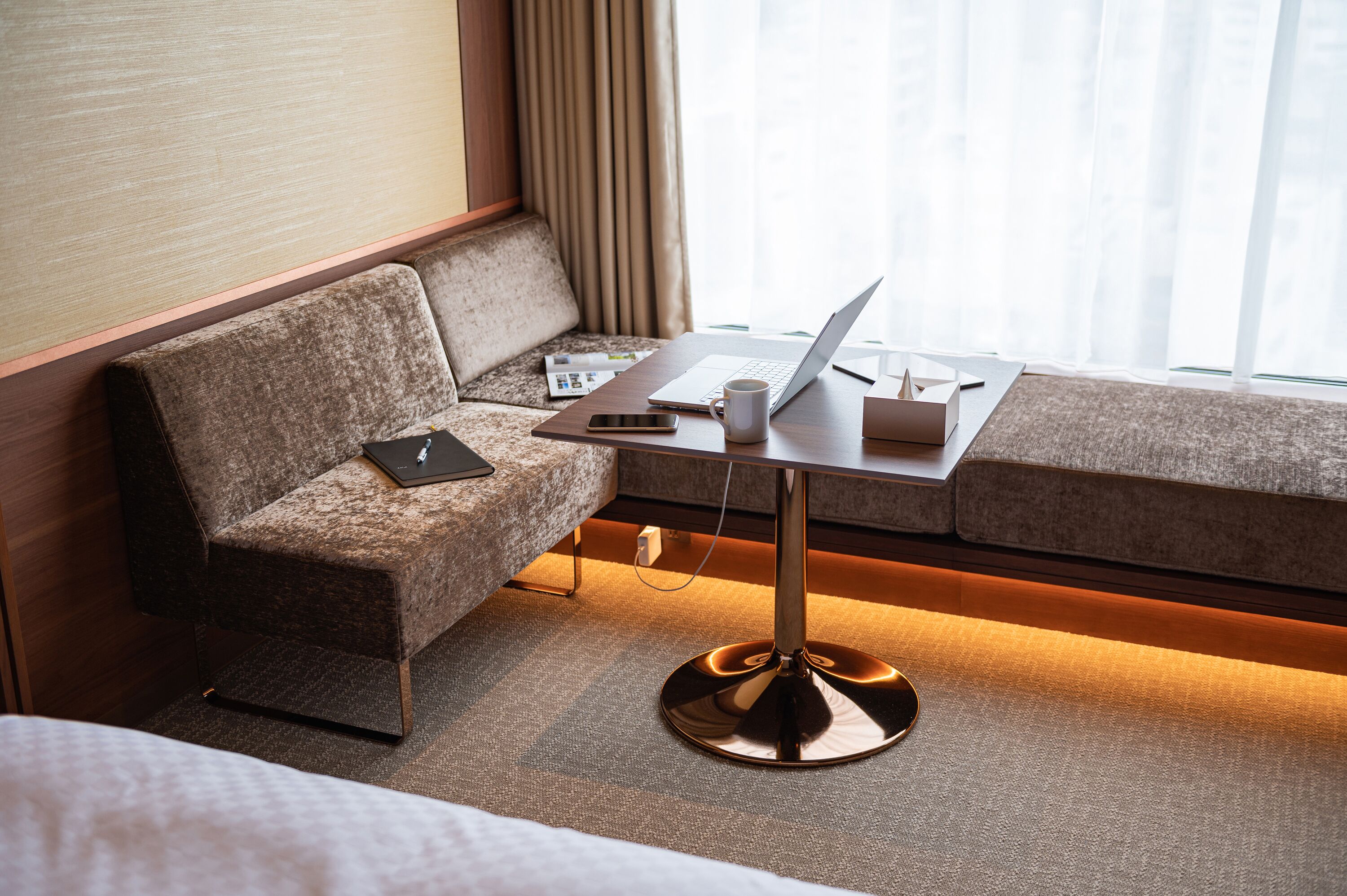Una habitación de hotel moderna con un sofá, una mesita con una computadora portátil, un teléfono inteligente y una taza.