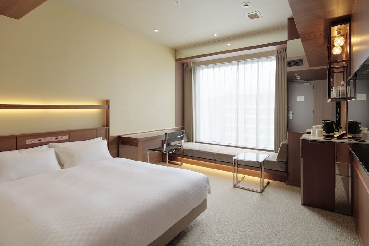 A hotel room with a large bed, a desk, a chair, a window with curtains, and a minibar.