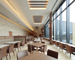 Un restaurant moderne avec de hauts plafonds, un éclairage encastré et de grandes fenêtres offrant une vue sur la ville.