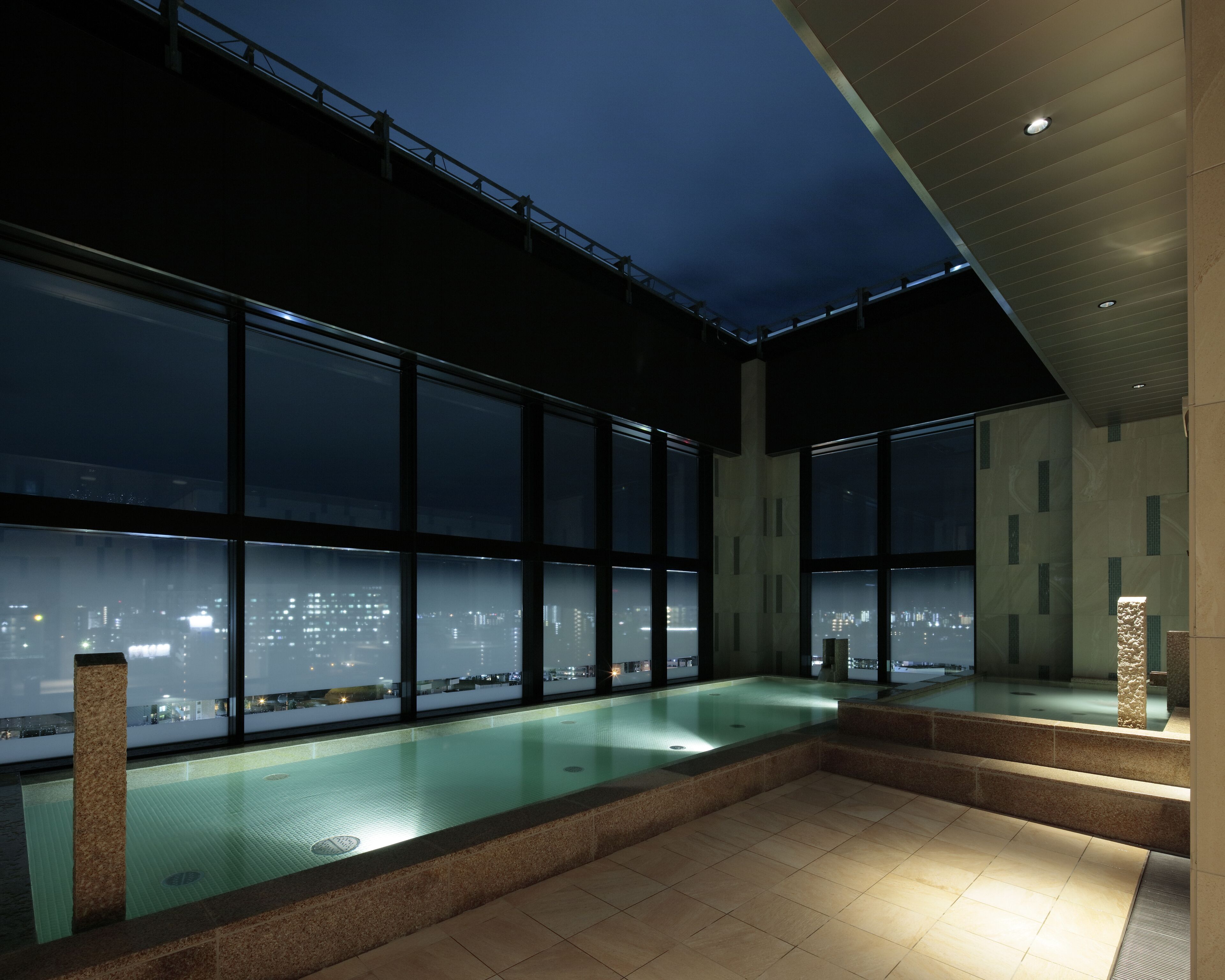 Piscina interior moderna com amplas janelas que dão para uma vista urbana noturna.