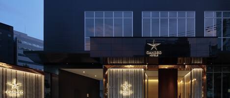 A modern hotel entrance with a star logo, large windows, and a well-lit facade.