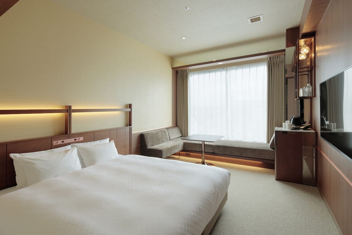 A hotel room with a large bed, a sofa, a small table, and a TV.