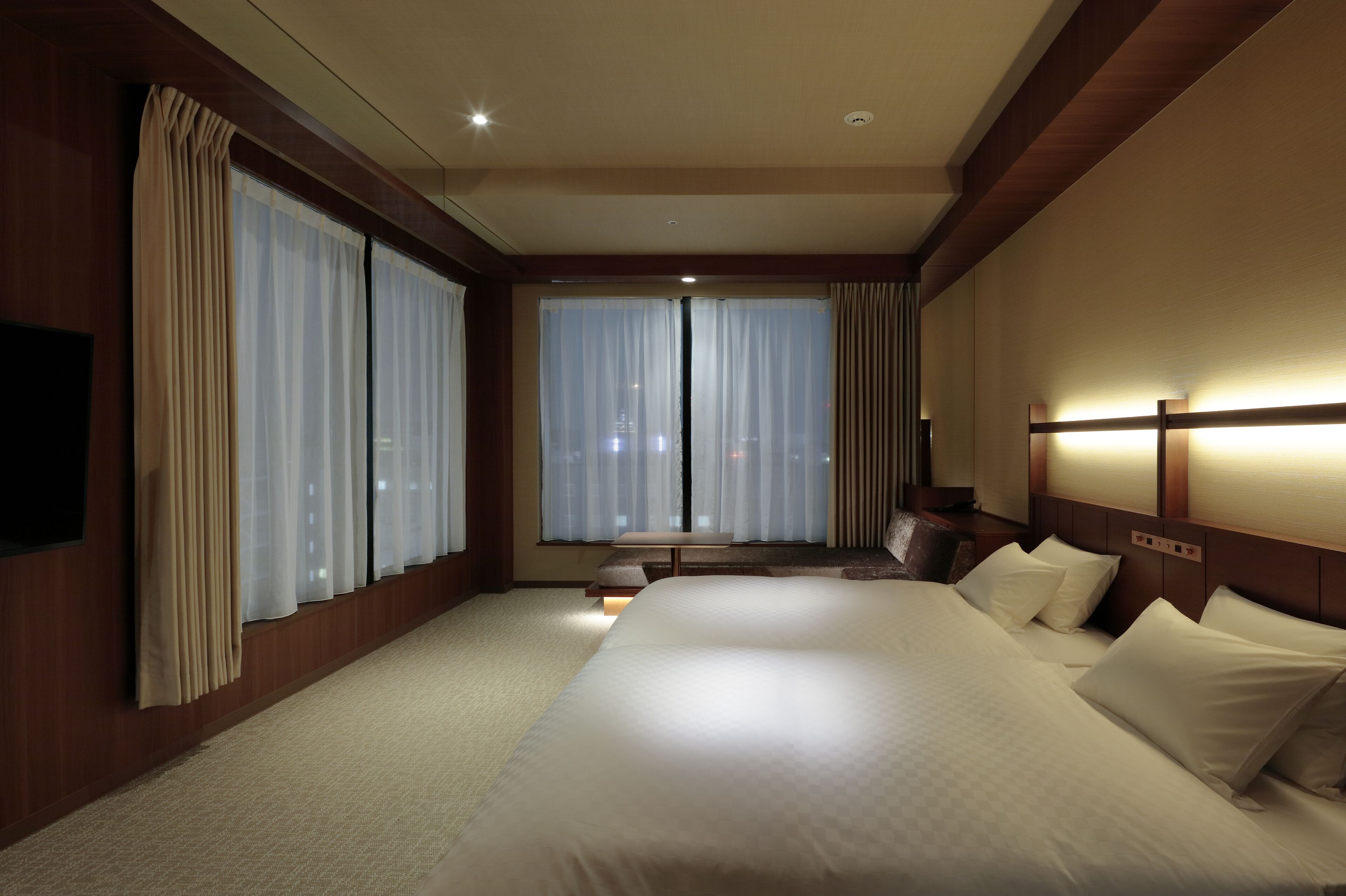 Habitación de hotel con una cama grande, una mesita de noche, un televisor y una ventana con cortinas.