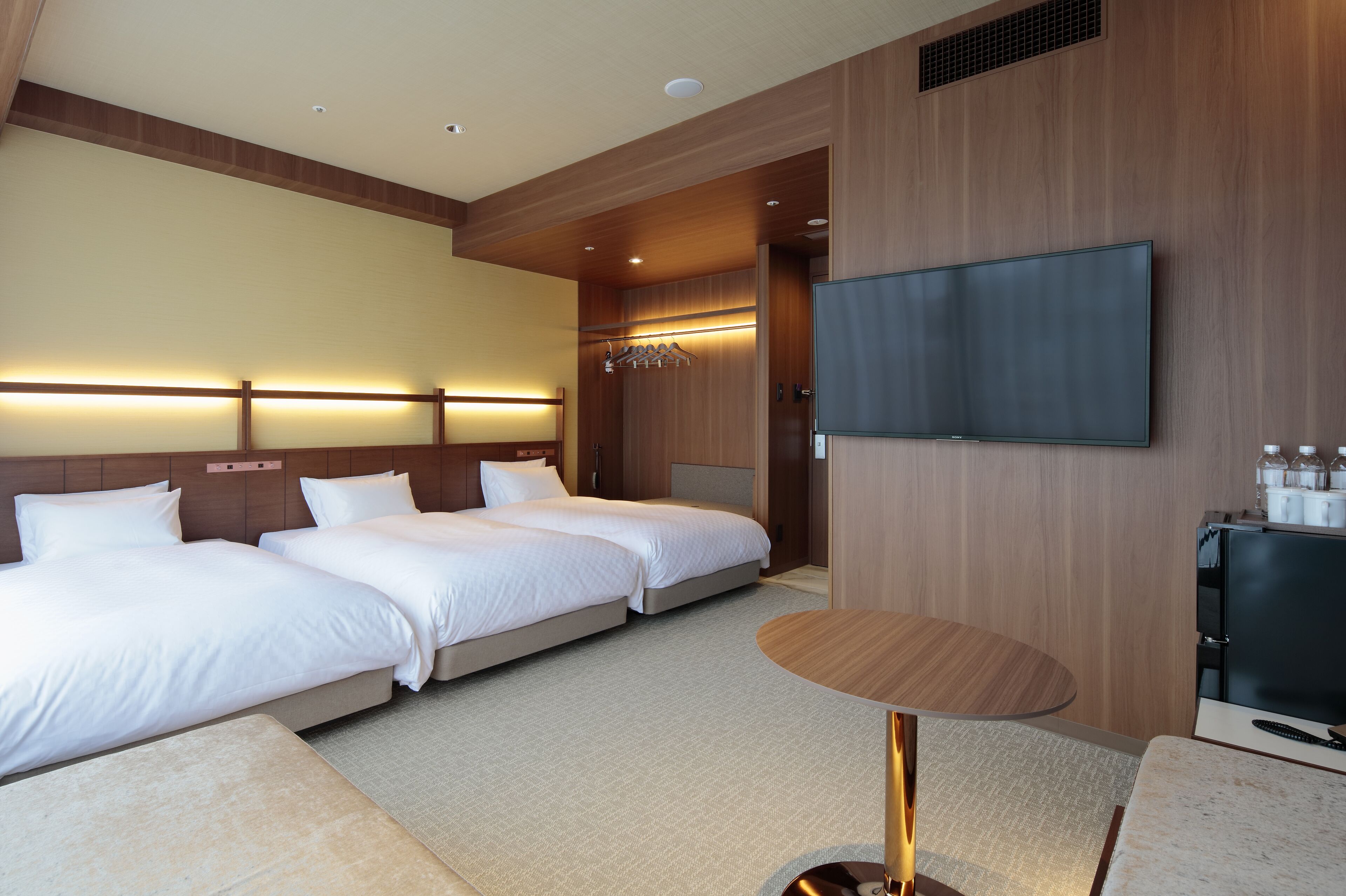 A hotel room with two beds, a TV, a small table, and a minibar.