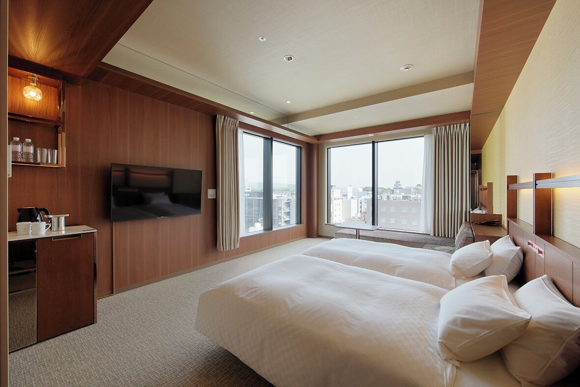 A hotel room with a large bed, a TV, a desk, and a city view.