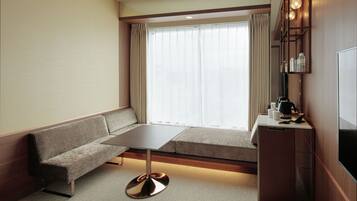 A modern hotel room with a sofa, a small table, a TV, and a minibar.