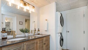 Een badkamer met twee wastafels, een spiegel, een handdoekhouder, een plant in pot en een wasmachine.