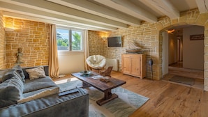 A cozy living room with a stone wall, a wooden ceiling, a sofa, a coffee table, a TV, and a stone fireplace.