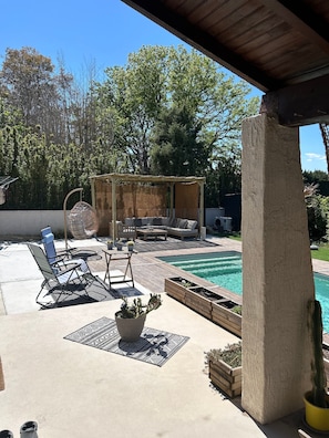 Un espace extérieur abrité comprenant une piscine, des chaises longues, une terrasse en bois et une pergola dotée d’un toit en treillis.