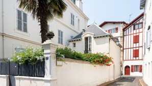 Une rue étroite avec un immeuble blanc, une clôture en métal noir et une porte rouge.