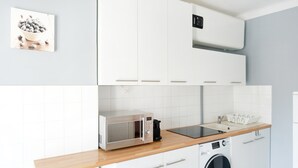 Une cuisine avec des meubles blancs, un four à micro-ondes, un lave-linge et un plan de travail en bois.