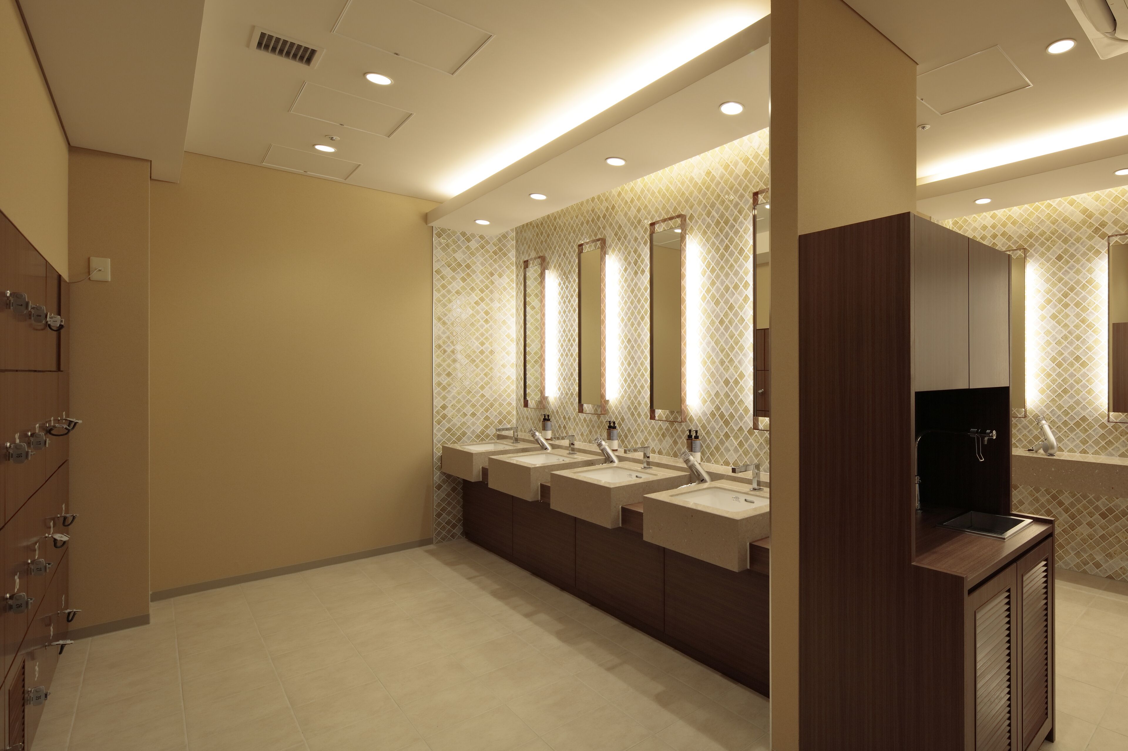 Une salle de bain moderne dotée de plusieurs lavabos, de miroirs et d’un espace coiffeuse.