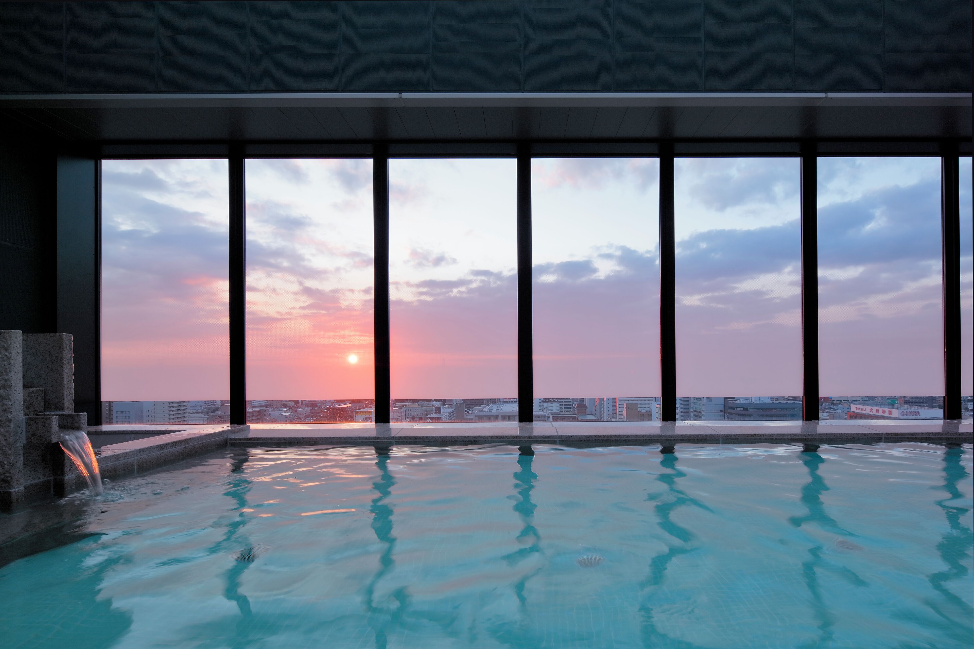 A rooftop infinity pool with a sunset view through large windows.