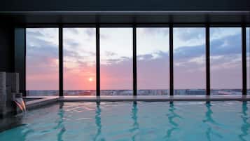 A rooftop infinity pool with a sunset view through large windows.
