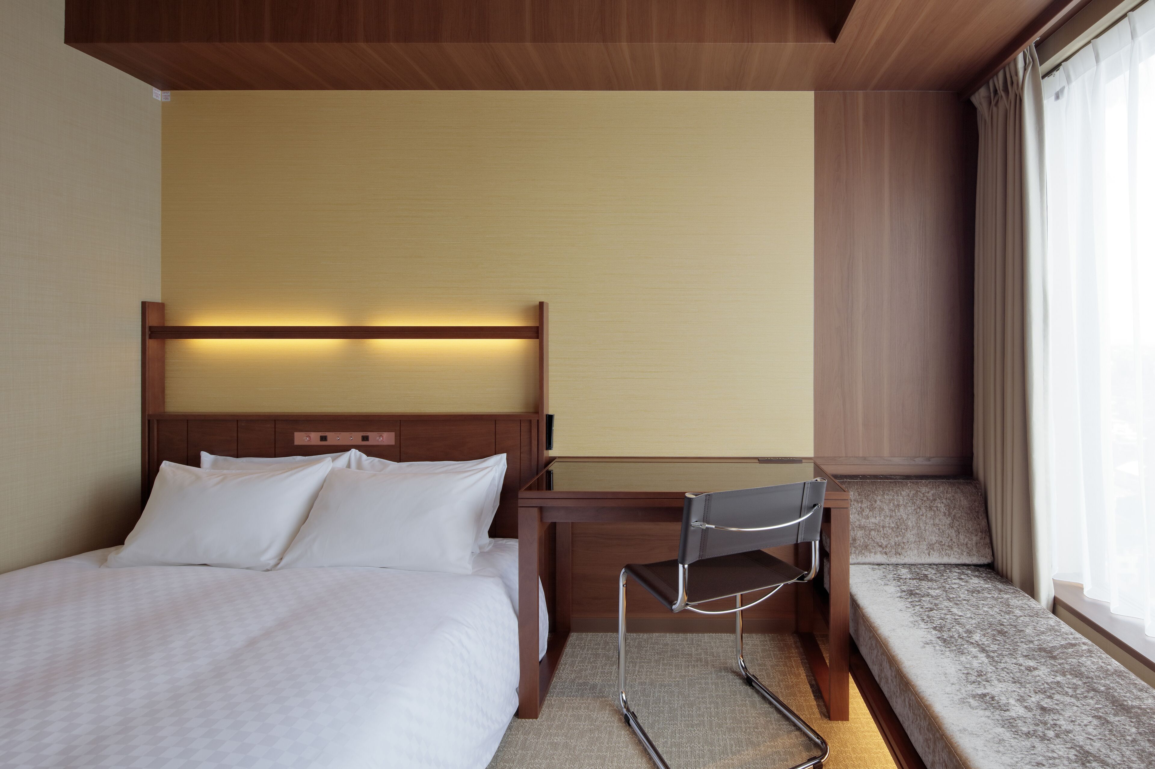 A hotel room with a bed, a desk, and a window with curtains.