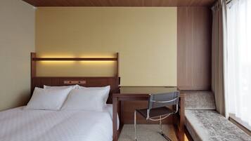 Quarto de hotel com cama, escrivaninha e janela com cortinas.
