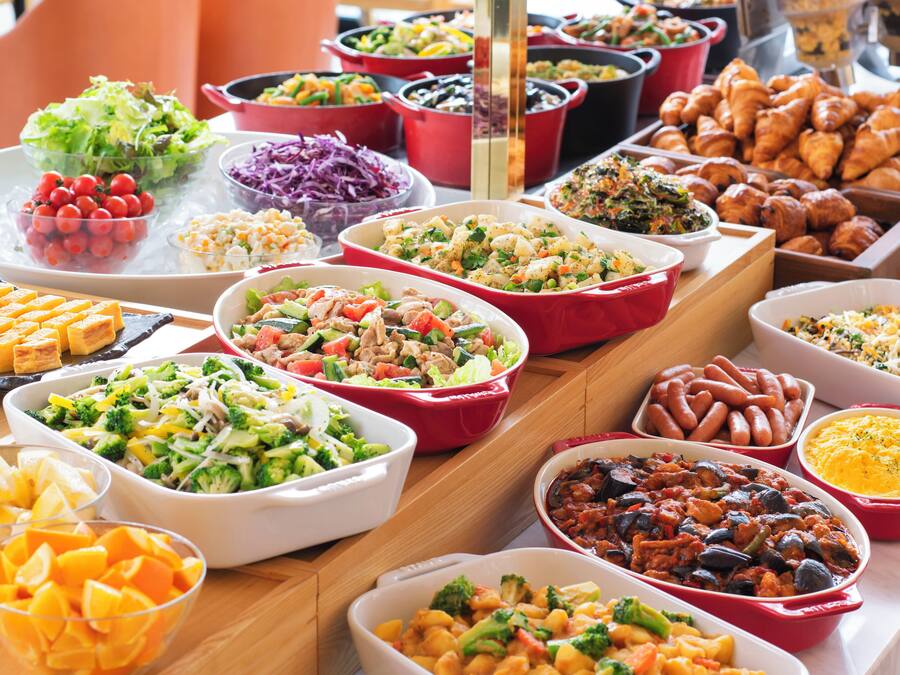 A buffet table with various dishes including salads, vegetables, and baked goods.