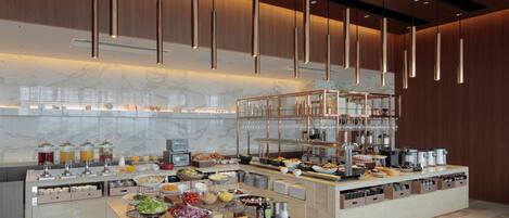 A modern buffet setup with various food items and beverages, wooden paneling, and hanging pendant lights.