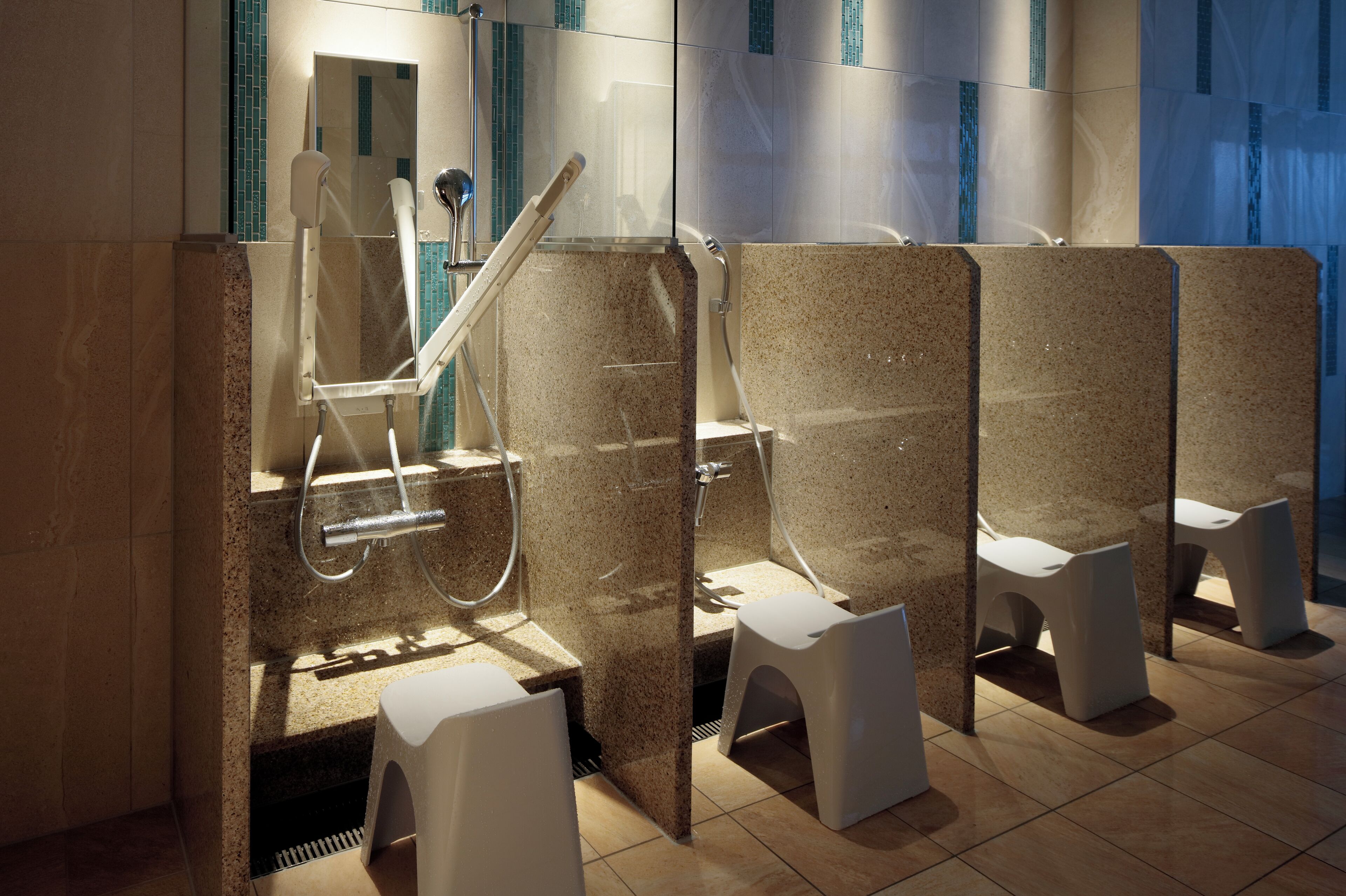 Un baño moderno con cabinas de ducha separadas, cada una con un cabezal de ducha manual y un taburete.