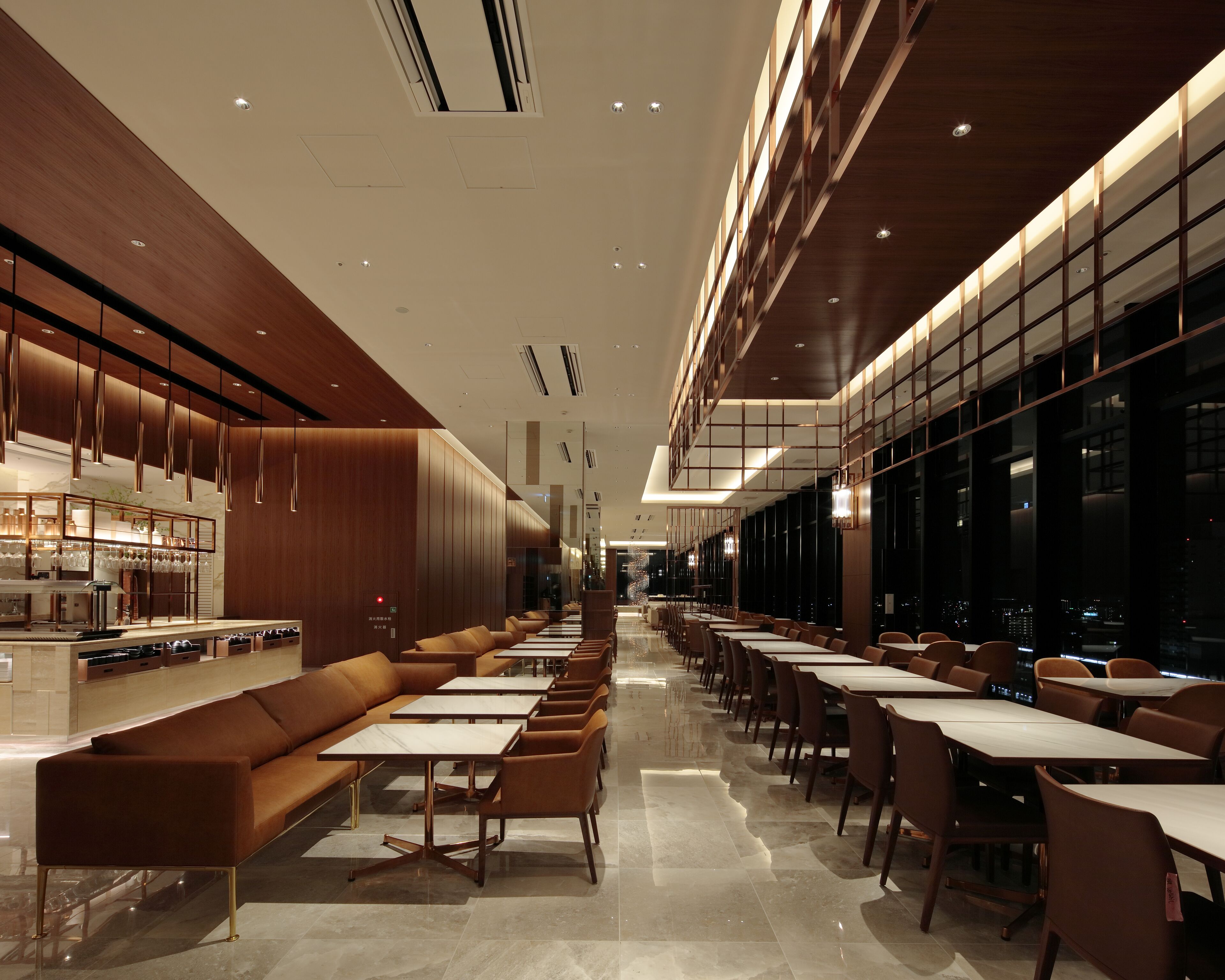 A modern restaurant with a long counter, cushioned seating, and a city view.