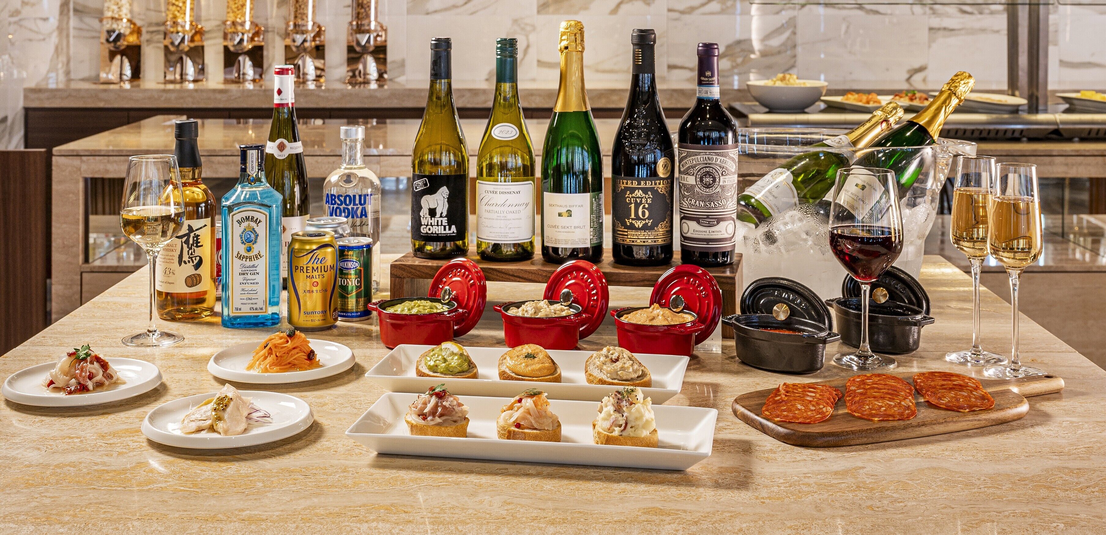 A bar area with various bottles of alcohol, glasses, and food items on a marble countertop.