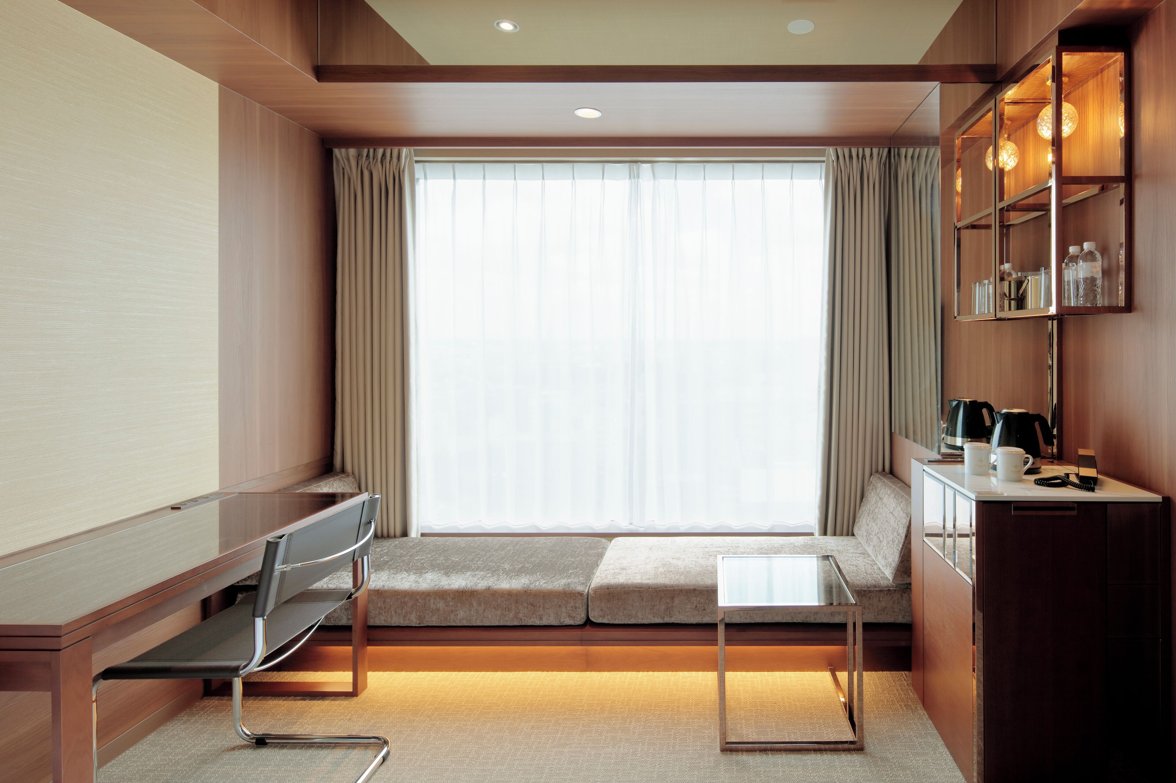 Una habitación de hotel moderna con sofá, una mesita, escritorio y estantería empotrada con iluminación.