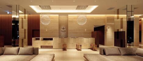 A modern hotel lobby with a reception desk, seating area, and decorative lighting.