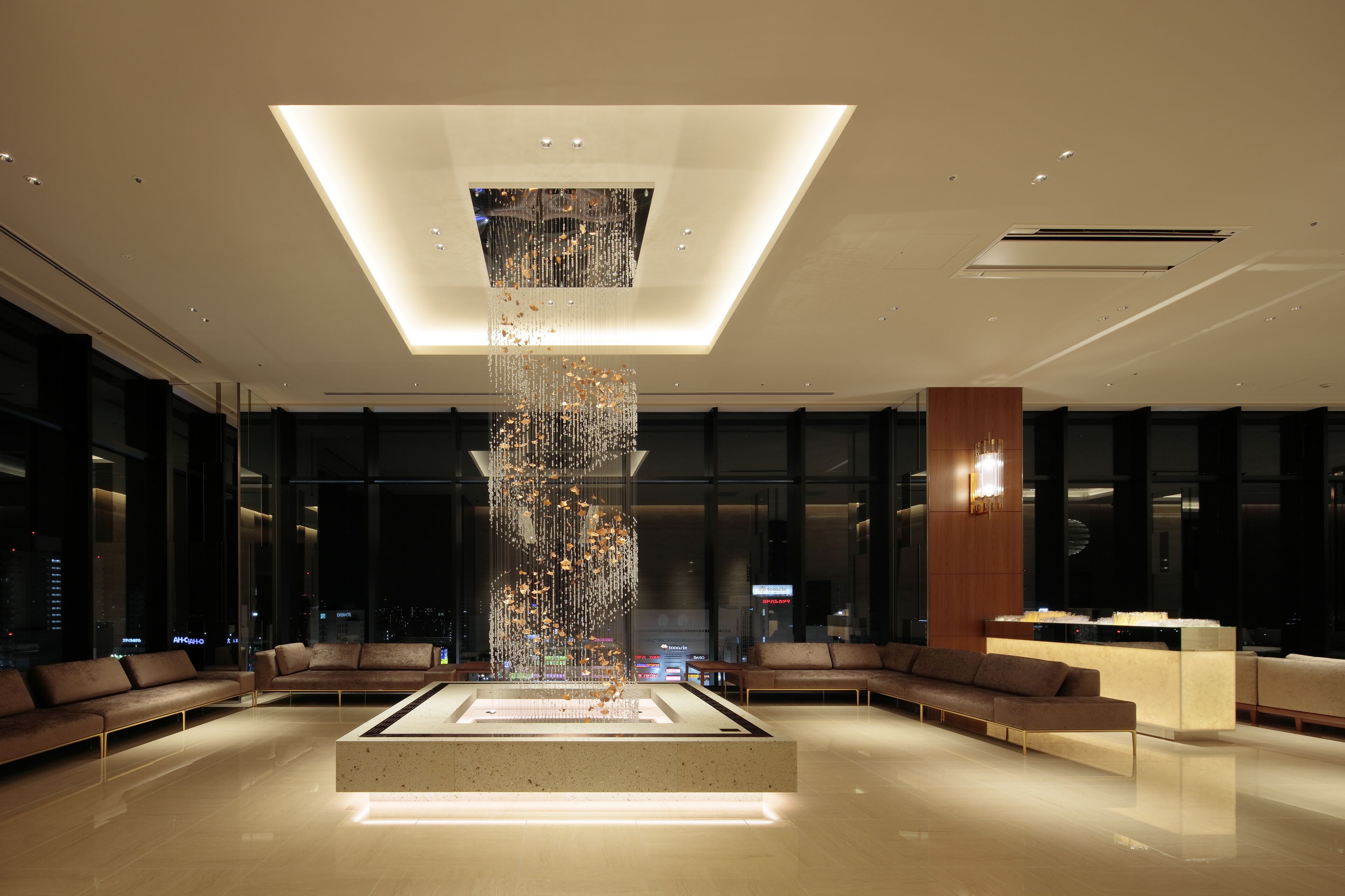 Un hall d’entrée moderne doté d’un élément décoratif central en eau, d’espaces de détente et de grandes fenêtres offrant une vue sur la ville.