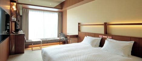 A hotel room with a large bed, a desk with a chair, a TV, and a window with curtains.