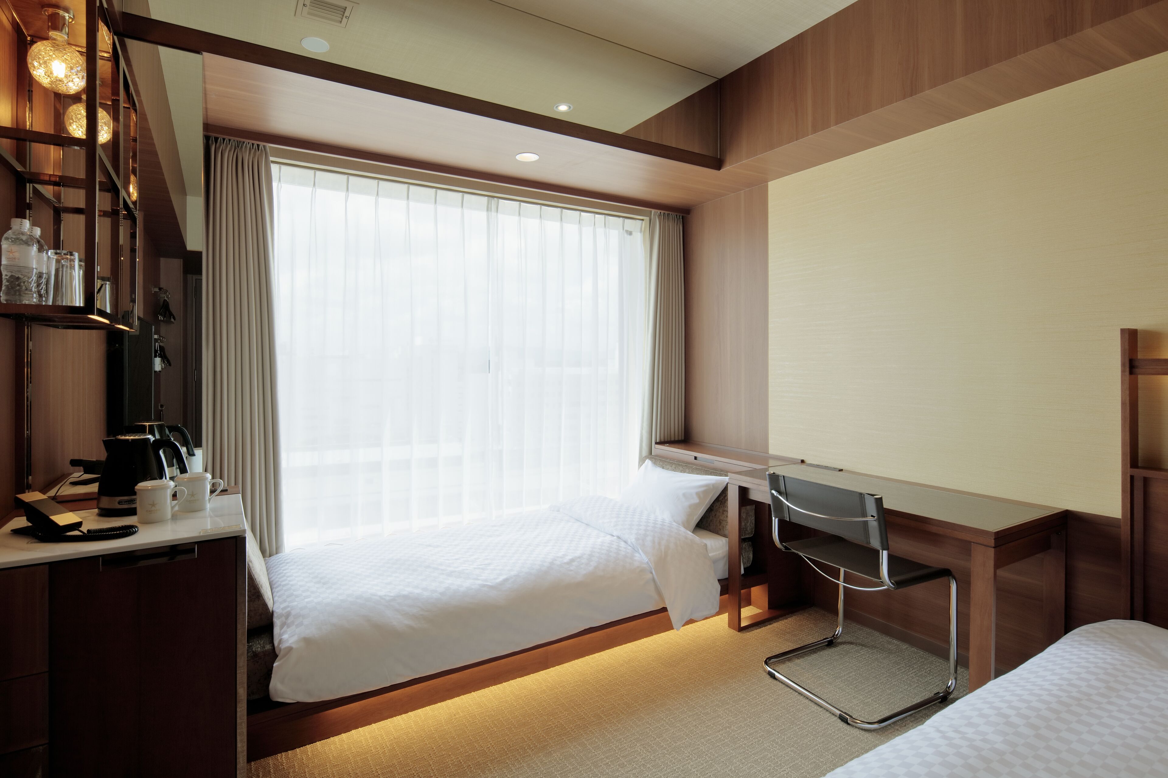 A hotel room with a bed, a desk with a chair, a coffee maker, and a window with curtains.