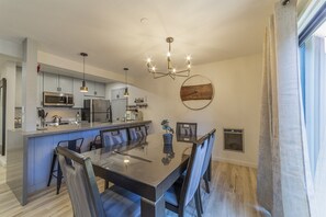 Una cucina moderna con elettrodomestici in acciaio inossidabile, un'area pranzo con tavolo e sedie in vetro e una lampada a sospensione.