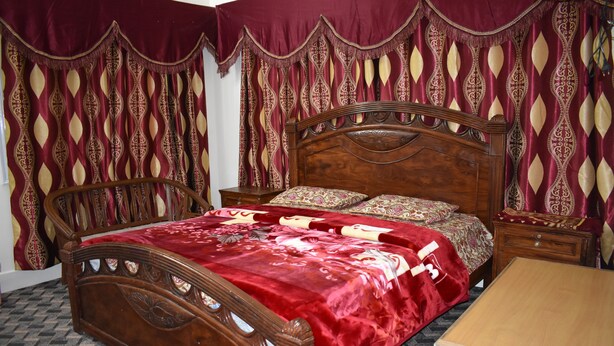 A wooden bed with a red bedspread, a matching nightstand, and a wooden table. - Snow Land Hotel Kaghan (Balakot)