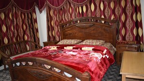 A wooden bed with a red bedspread and matching pillows, flanked by ornate curtains and a wooden nightstand. - Snow Land Hotel Kaghan (Balakot)