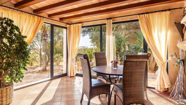 Un patio cubierto con una mesa, sillas, ventanas amplias y una planta en maceta.