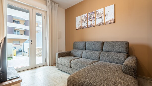 A living room with a grey sofa, a television on a wooden stand, and a sliding glass door leading to an outdoor area. - Holiday Home Casa Mattia with Terraces, Garden & Wi-Fi (Quartu Sant'Elena)