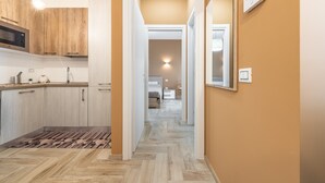 A modern kitchen with wooden cabinets, a microwave, and a light fixture. A hallway leads to a bedroom with a bed and a nightstand. - Holiday Home Casa Mattia with Terraces, Garden & Wi-Fi (Quartu Sant'Elena)