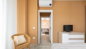 A hotel room with a bed, a television on a dresser, a wicker chair, and a hallway leading to another room. - Holiday Home Casa Mattia with Terraces, Garden & Wi-Fi (Quartu Sant'Elena)