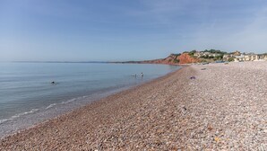 Una playa de adoquines con aguas tranquilas, cielo despejado y edificios al fondo.
