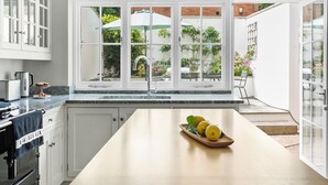 Una cocina moderna con una isla grande, armarios blancos y vistas a un jardín a través de ventanas amplias.