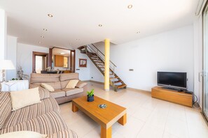 En moderne stue med sofa, sofabord, TV, trappe og et køkkenområde.